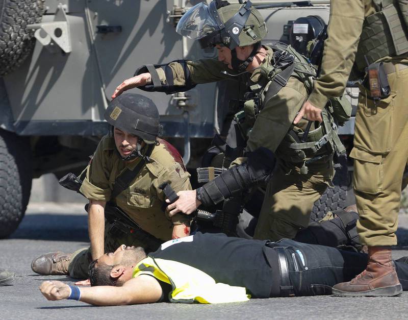 En israelisk soldat böjer sig över den man som knivskurit honom i Hebron för några dagar sedan. Mannen sköts senare ihjäl.