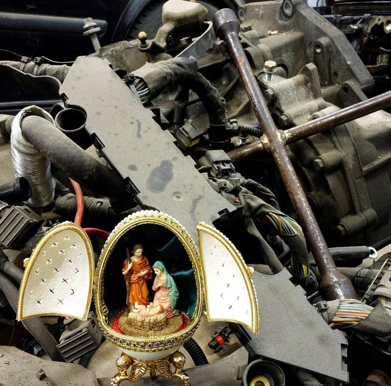 Julkrubba från paret Josefssons samling, omringad av en bilmotor och ett fälgkors. Bilden kommer från boken ”Jesus ETC” där julkrubban och dess budskap placeras i vår vardagliga miljö. 