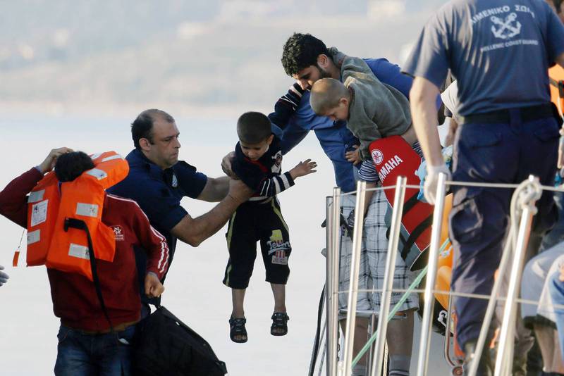 En man räcker över sin son till en besättningsman från en båt från den grekiska kustbevakningen nära den grekiska ön Lesvos. 