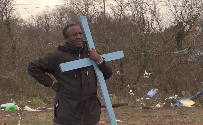 Prästen Teferi Shuremo håller ett kors - det enda som blev kvar när kyrkan i flyktinglägret i Calais jämnades med marken måndag morgon.