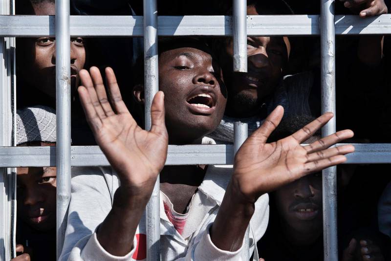En emigrant gestikulerar bakom gallret i en cell på ett häkte i Libyen.