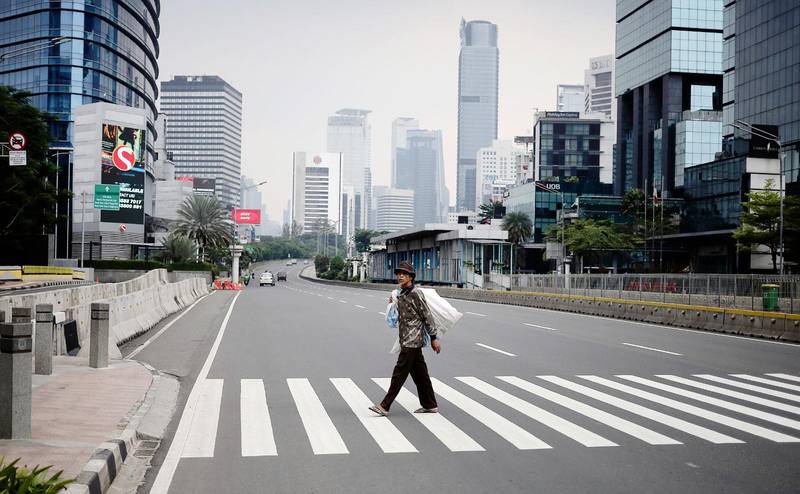 En man går över den i vanliga fall hårt trafikerade Sudirman Street i Indonesiens huvudstad Jakarta. En stad som drabbats hår under den pågående coronapandemin.
