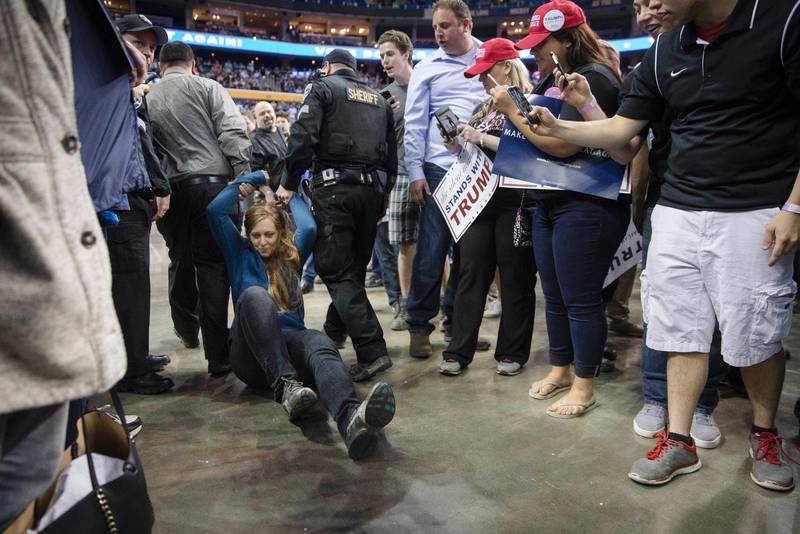 På bilden släpas en kvinna bort från ett kampanjmöte efter att ha protesterat mot Trump.