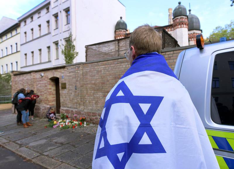 En person omsvept i Israels flagga står i närheten av blommor och ljus efter attacken mot en synagoga i tyska Halle i oktober 2019 där två personer miste livet under högtiden jom kippur.