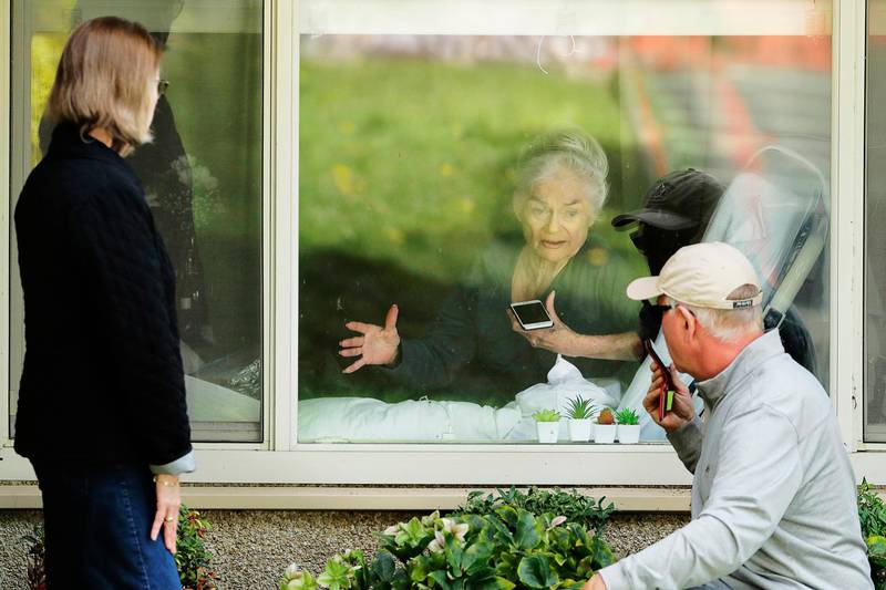 Judie Shape, center, who has tested positive for the new coronavirus, but isn't showing symptoms, visits through the window and on the phone with her daughter Lori Spencer, left, and her son-in-law Michael Spencer, Tuesday, March 17, 2020, at the Life Care Center in Kirkland, Wash., near Seattle. In-person visits are not allowed at the nursing home, which is at the center of the outbreak of the new coronavirus in the United States. (AP Photo/Ted S. Warren)  WATW129