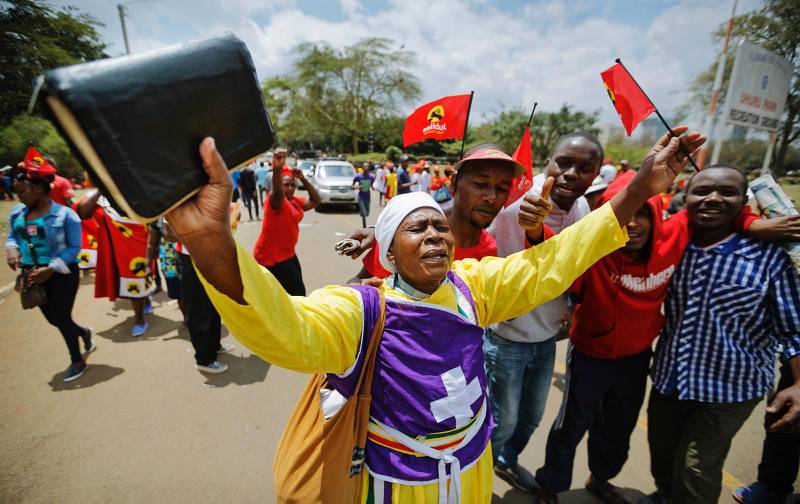 En kristen anhängare till sittande presidenten Uhuru Kenyatta med en bibel i ena handen och en flagga den andra på ett valmöte.