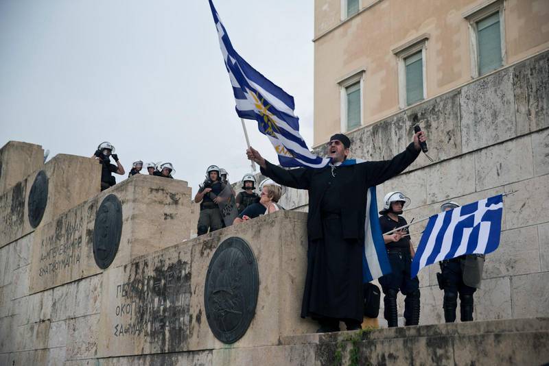 Grekisk-ortodoxa kyrkan i Grekland har protesterat mot avtalet. Här en munk som viftade med grekiska flaggan utanför Greklands parlament i lördags.