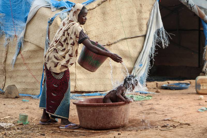 In this Thursday, May 14, 2020, photo, a mother who fled the north after her village was attacked by gunmen, washes her baby outside the tent in Nouna, Burkina Faso, where she now lives and depends on food handouts. Violence linked to Islamic extremists has spread to Burkina Faso's breadbasket region, pushing thousands of people toward hunger and threatening to cut off food aid for millions more. (AP Photo/Sam Mednick)  NAI502