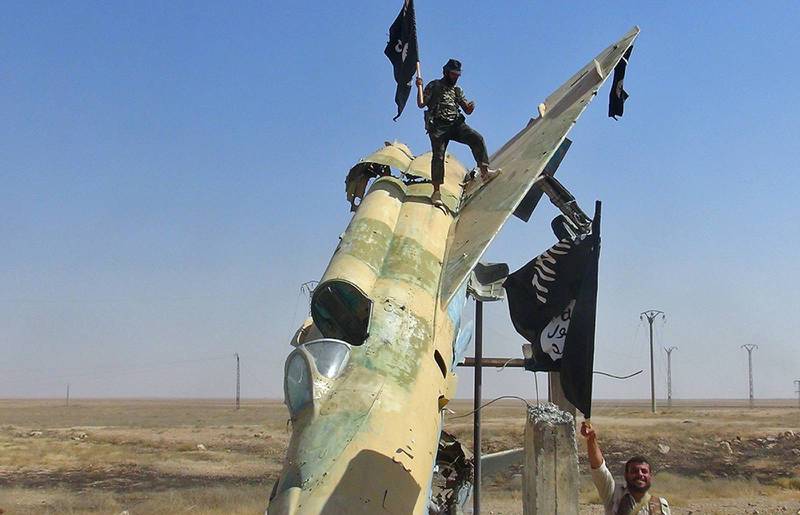 En IS-krigare viftar med en flagga vid ett nedskjutet syriskt flygplan.