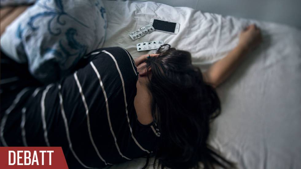 Anonym kvinna ligger i säng med två kartor piller och en mobil framför sig.